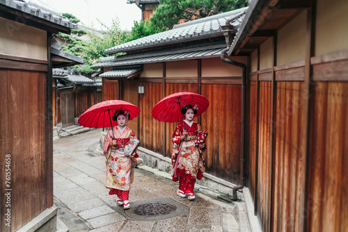 Kyoto's cultural tapestry comes alive as Geishas with red umbrellas navigate a rainy traditional Gion district photo