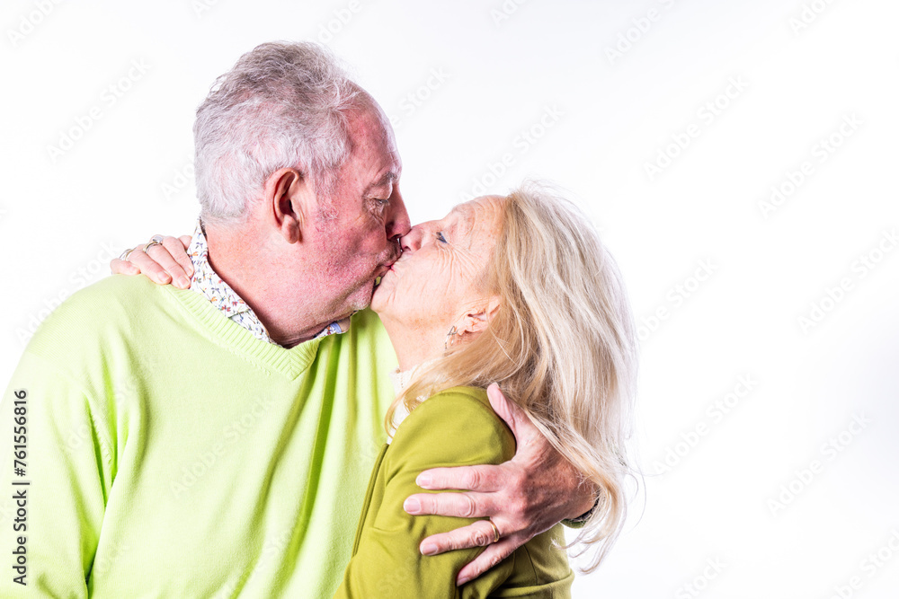 This heartwarming image captures a tender moment between a senior couple as they share a loving kiss. Both are dressed in vibrant sweaters, with a white background that accentuates the intimacy and This heartwarming image captures a tender moment between a senior couple as they share a loving kiss. Both are dressed in vibrant sweaters, with a white background that accentuates the intimacy and