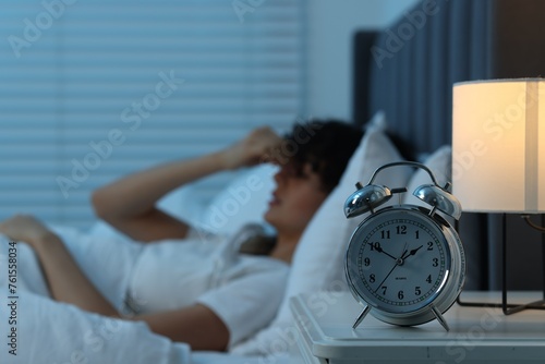 Young woman suffering from headache in bed at night, focus on alarm clock