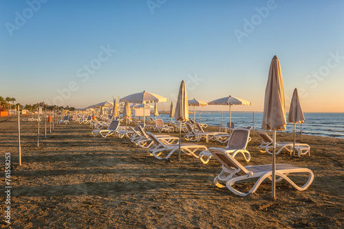 View of the Larnaca sandy beach at sunrise, tourist resort, Cyprus. Scenic seascape with beach umbrellas and sun loungers, travel background, summer holidays concept
