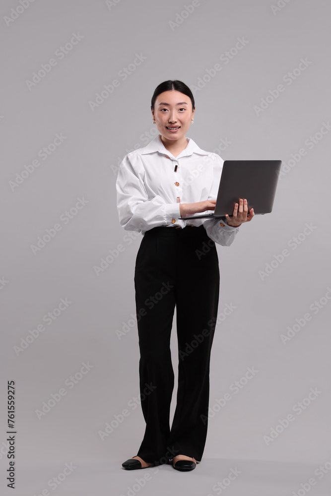 Full length portrait of smiling businesswoman with laptop on grey background Full length portrait of smiling businesswoman with laptop on grey background