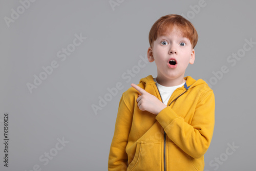 Obraz na płótnie Surprised little boy pointing at something on grey background, space for text