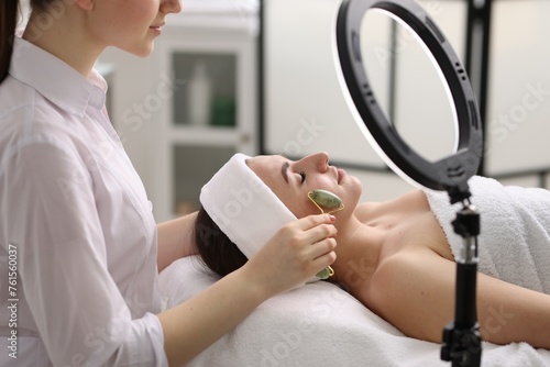 Cosmetologist making face massage with roller to client in clinic  closeup