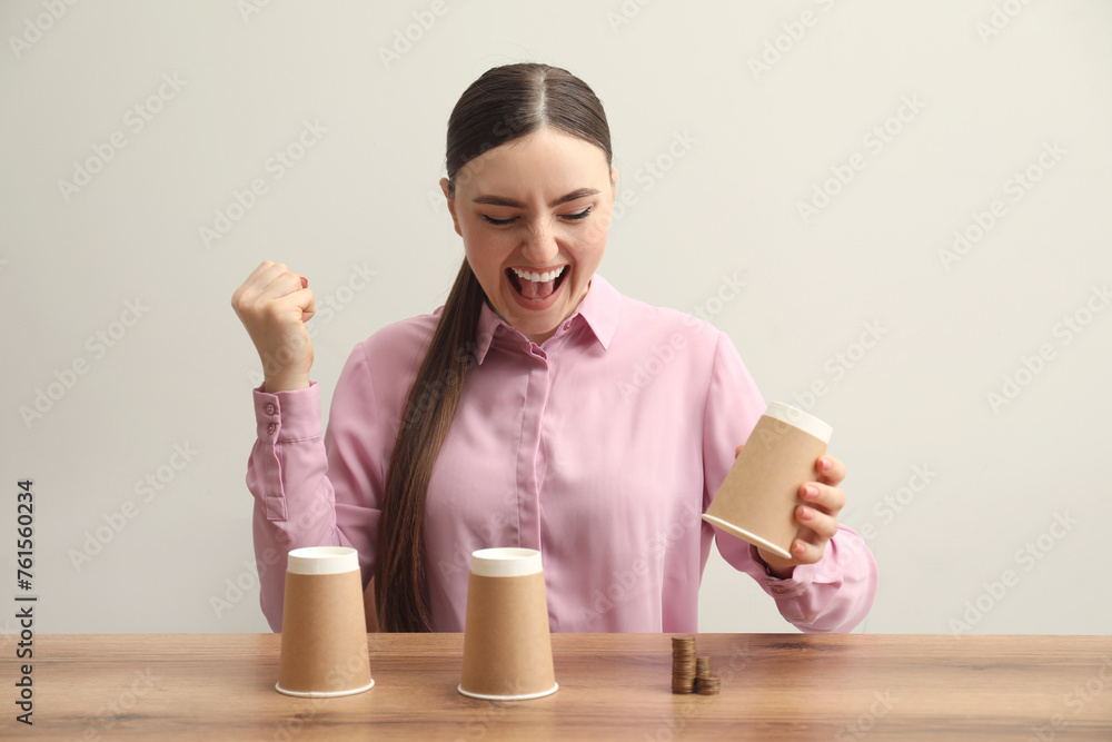 Shell game. Emotional woman showing stack of coins under cup at wooden table Shell game. Emotional woman showing stack of coins under cup at wooden table