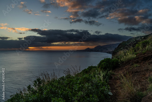A serene view of a Village rocky coast , under a dusk sky with fluffy clouds Colorful sunset at Caniço, Madeira island, Portugal