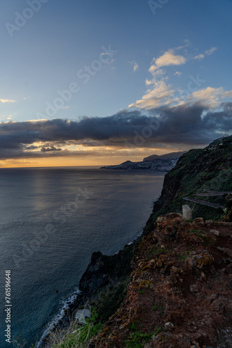 A serene view of a Village rocky coast , under a dusk sky with fluffy clouds Colorful sunset at Caniço, Madeira island, Portugal