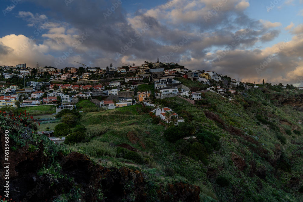 A serene view of a Village rocky coast , under a dusk sky with fluffy clouds Colorful sunset at Caniço, Madeira island, Portugal	