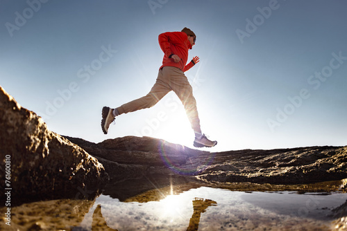 Running male silhouette athlete is running above a puddle early in morning. Tranquil scene with reflection in water