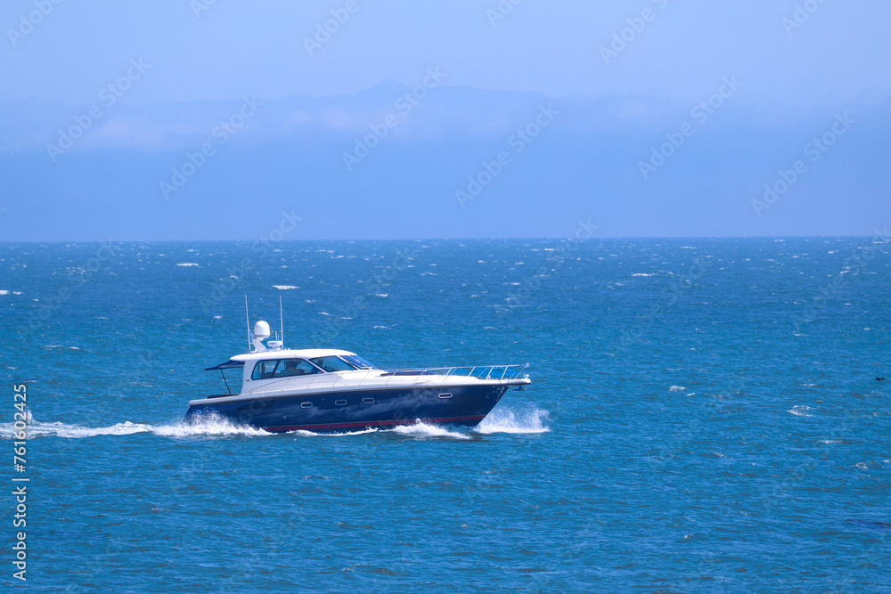 A side view of a beautiful motorboat with blue details sailing across the sea, making waves in the water. The boat is speeding along coastal waters. A side view of a beautiful motorboat with blue details sailing across the sea, making waves in the water. The boat is speeding along coastal waters.