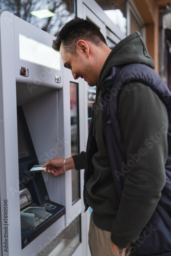 A one young man withdrawing money on ATM with credit card in the city