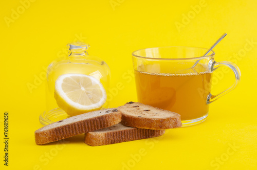 Cup of tea with rusks and lemon on yellow background