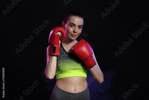 Portrait of beautiful woman wearing boxing gloves in color lights on black background