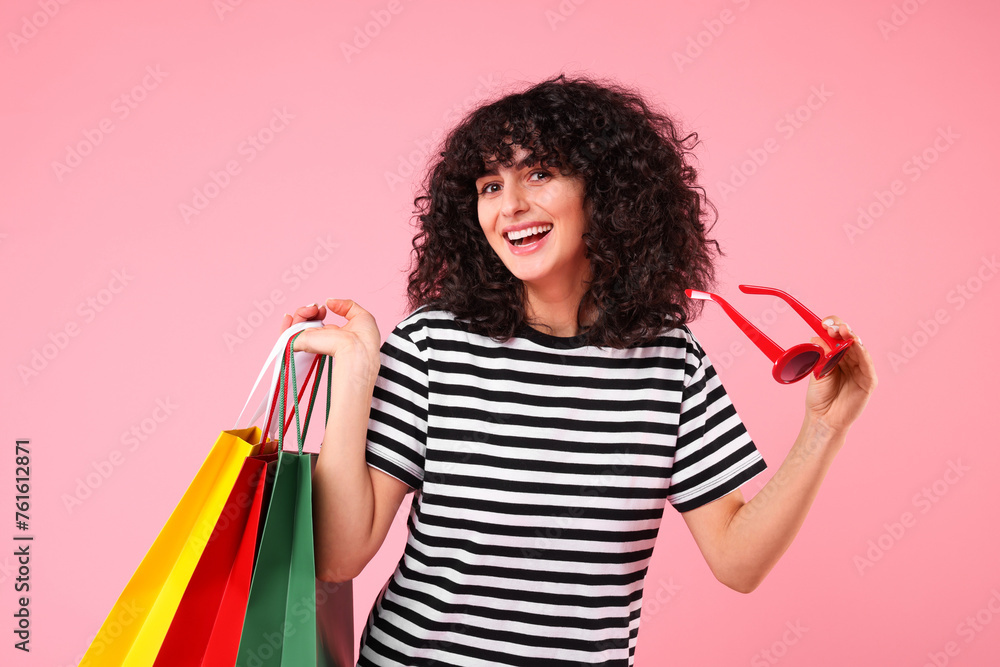 Happy young woman with shopping bags and stylish sunglasses on pink background Happy young woman with shopping bags and stylish sunglasses on pink background