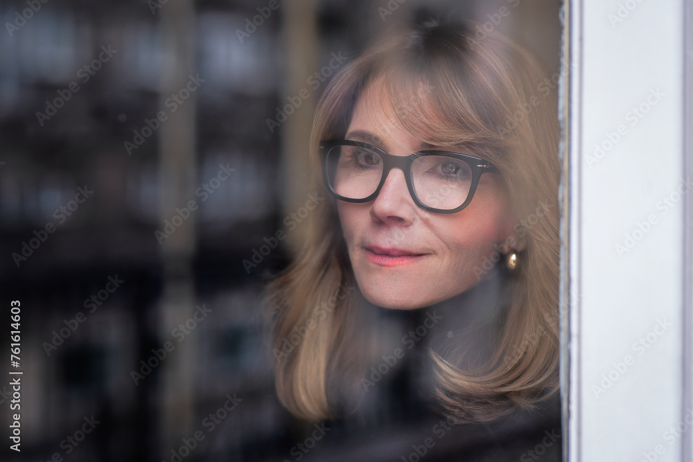 Headshot of an attractive mid aged woman standing behind the glass window and daydreaming Headshot of an attractive mid aged woman standing behind the glass window and daydreaming