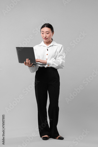 Full length portrait of businesswoman with laptop on grey background