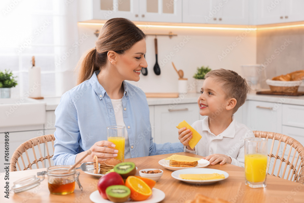 Mother and her cute little son having breakfast at table in kitchen