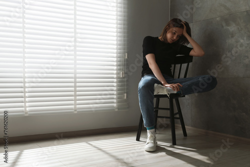 Sad young woman sitting on chair at home, space for text