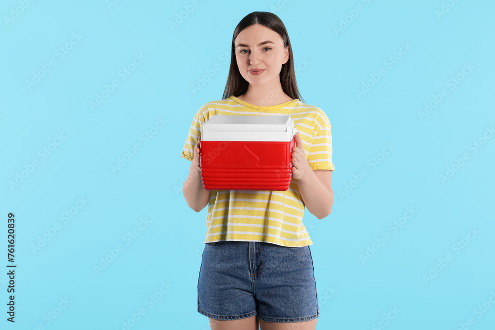Beautiful young woman with plastic cool box on light blue background Beautiful young woman with plastic cool box on light blue background