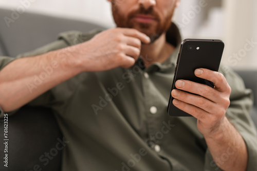 Handsome man using smartphone on sofa at home, closeup
