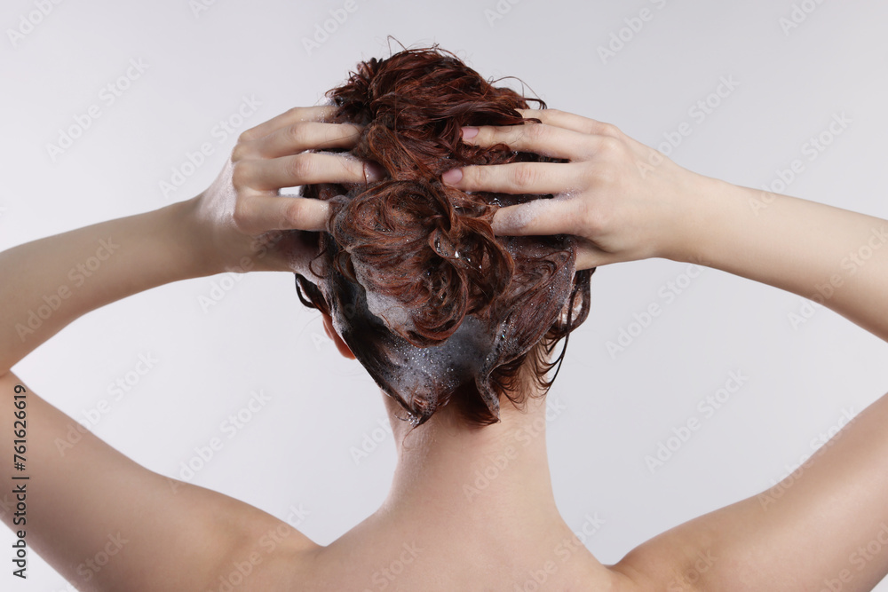 Naklejka premium Young woman washing her hair with shampoo on light grey background, back view