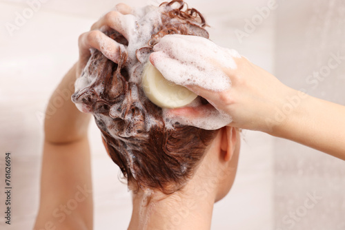 Young woman washing her hair with solid shampoo bar in shower, back view