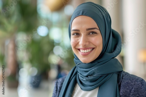 A smiling woman wearing a hijab, giving a friendly and open expression, set against a blurred indoor background that suggests a corporate or educational setting © romanets_v