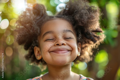 A young girl with a big smile, eyes tightly closed, and her hair styled in two large puffs, conveying a feeling of pure happiness and carefree joy