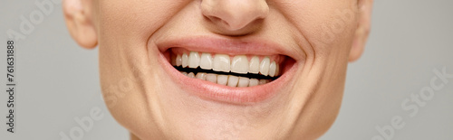 cropped banner of happy woman exuding joyful and healthy smile on grey background, white teeth