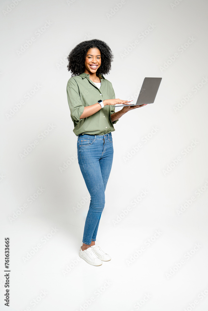Captured in a full-length shot, an African-American woman with a joyful expression using the laptop, showcasing the versatility of modern wireless devices that allow for mobility and flexibility Captured in a full-length shot, an African-American woman with a joyful expression using the laptop, showcasing the versatility of modern wireless devices that allow for mobility and flexibility