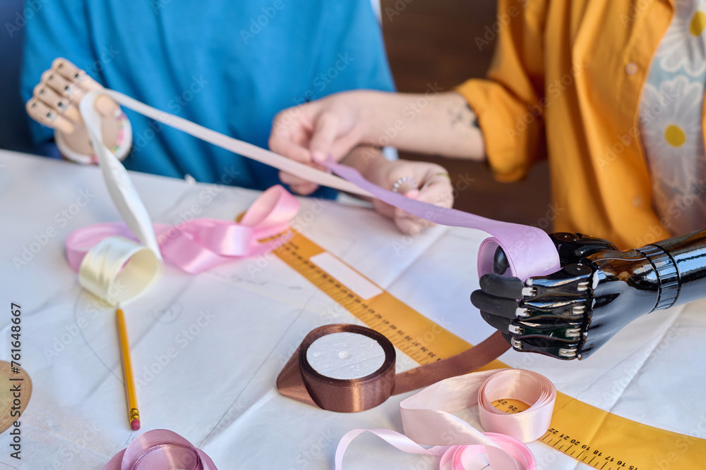 Close up of two girls with disability working in inclusive atelier studio and holding ribbons with prosthetic hands copy space Close up of two girls with disability working in inclusive atelier studio and holding ribbons with prosthetic hands copy space