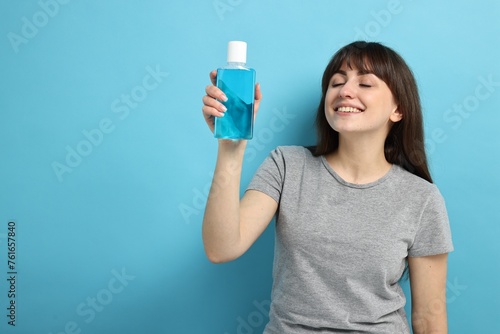 Young woman with mouthwash on light blue background, space for text © New Africa