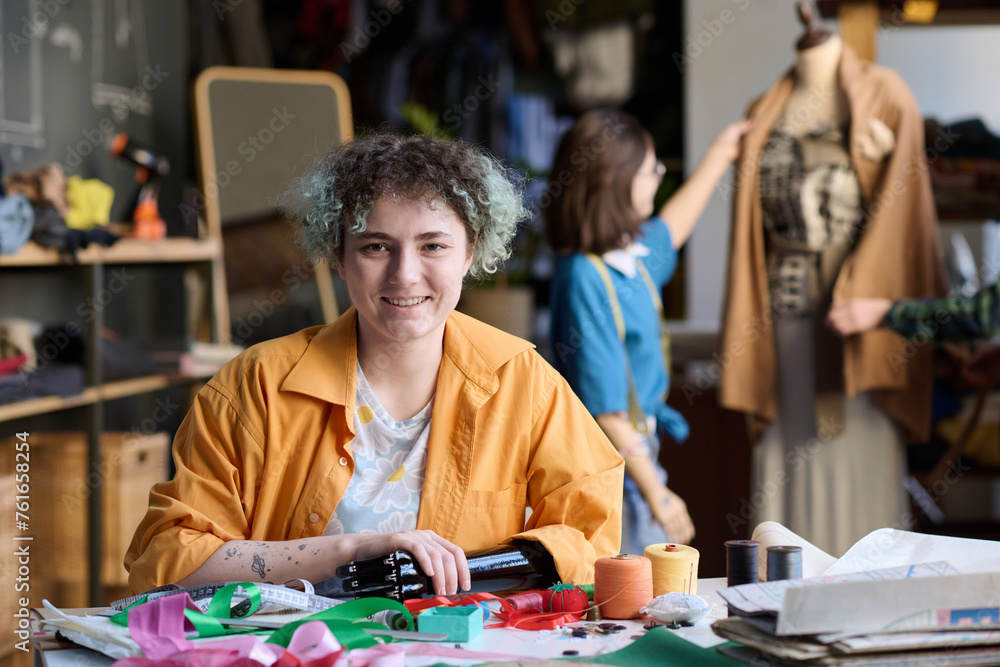 Fototapeta premium Portrait of young woman with arm prosthetic smiling at camera in atelier workshop copy space