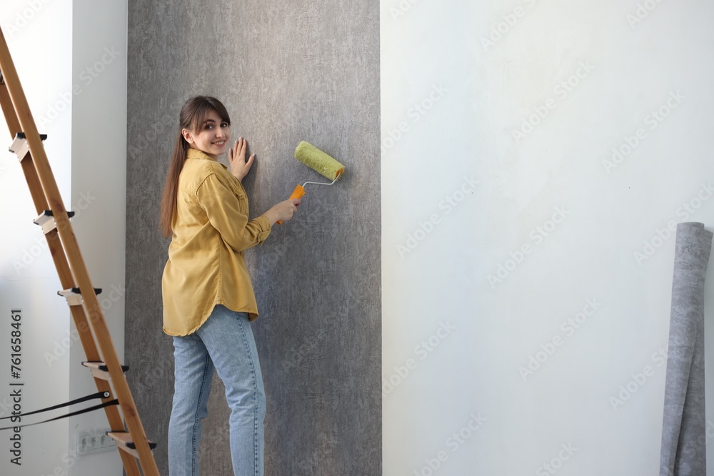 Woman hanging stylish gray wallpaper in room Woman hanging stylish gray wallpaper in room