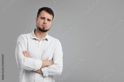 Portrait of sad man with crossed arms on grey background, space for text