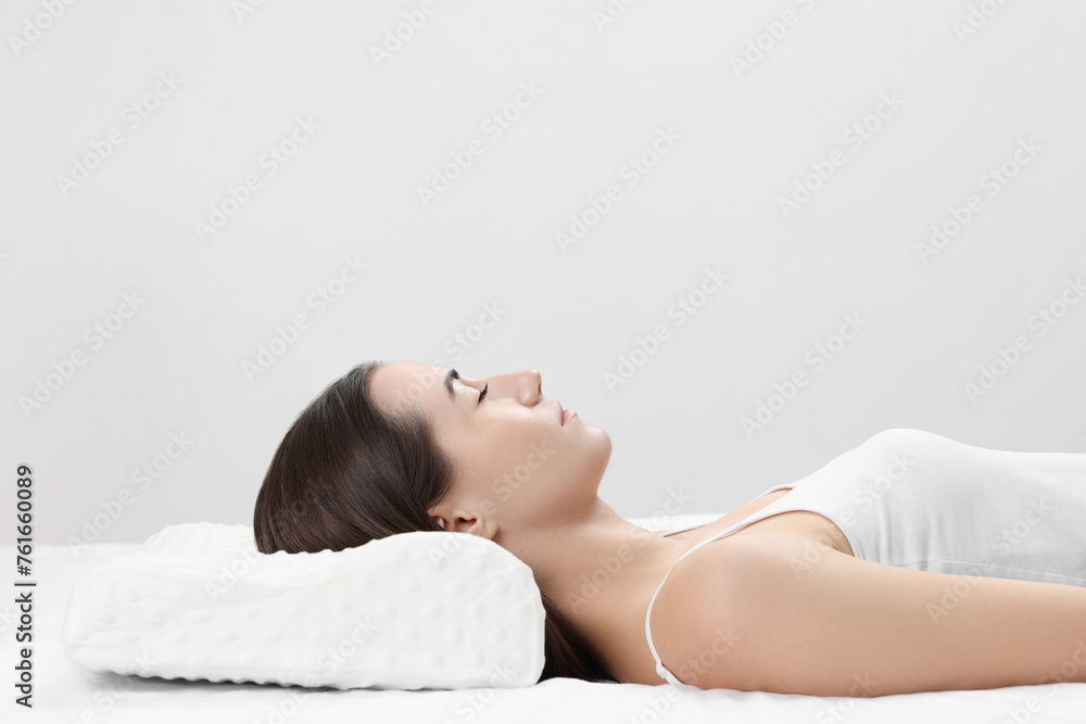 Woman sleeping on orthopedic pillow against light grey background, space for text Woman sleeping on orthopedic pillow against light grey background, space for text