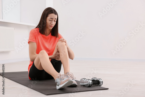 Young woman suffering from leg pain on exercise mat indoors, space for text