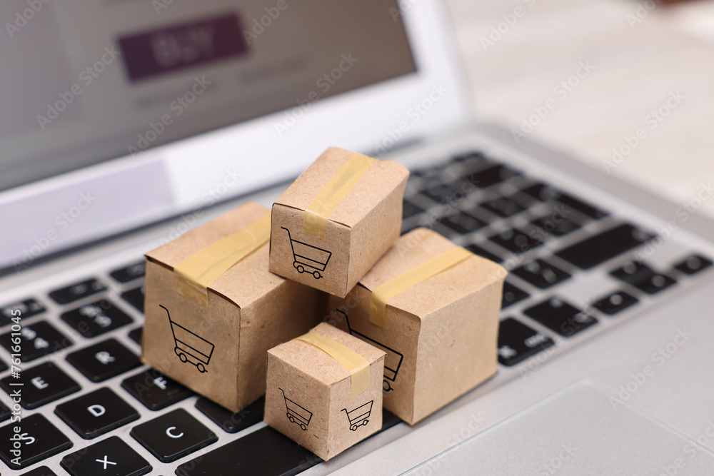 Fototapeta premium Internet store. Small cardboard boxes with shopping carts on laptop, closeup
