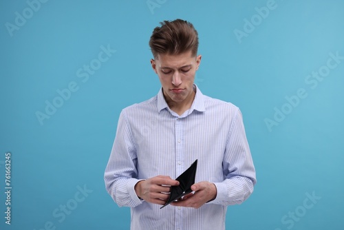 Upset man looking into empty wallet on light blue background