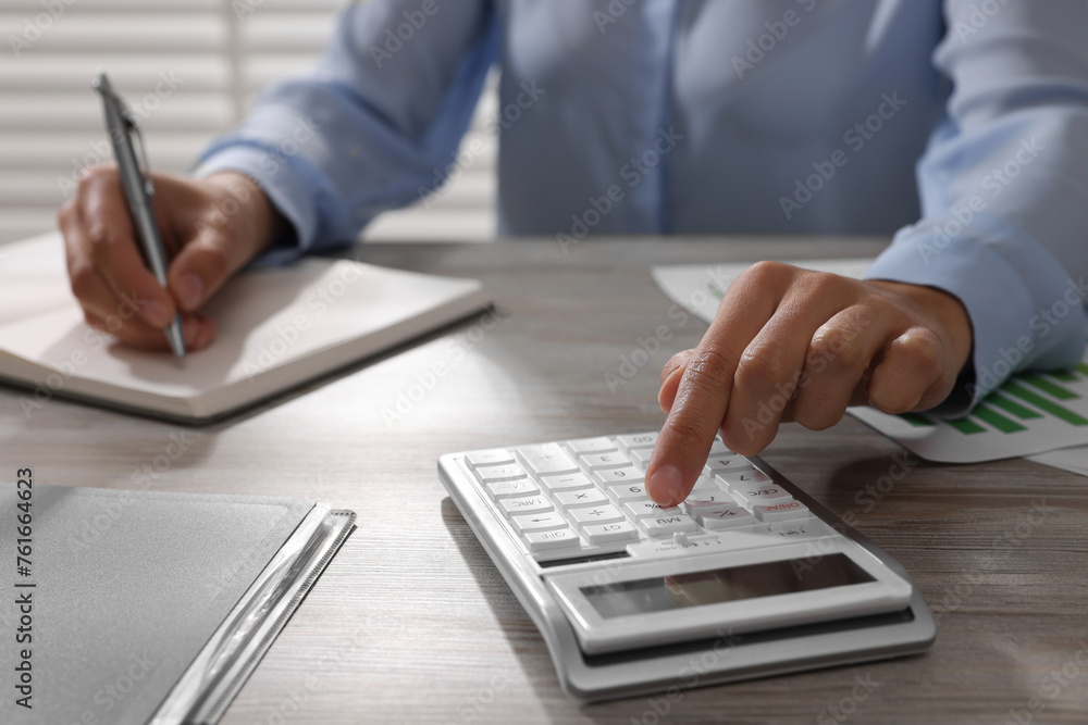 Woman using calculator at light wooden table in office, closeup Woman using calculator at light wooden table in office, closeup