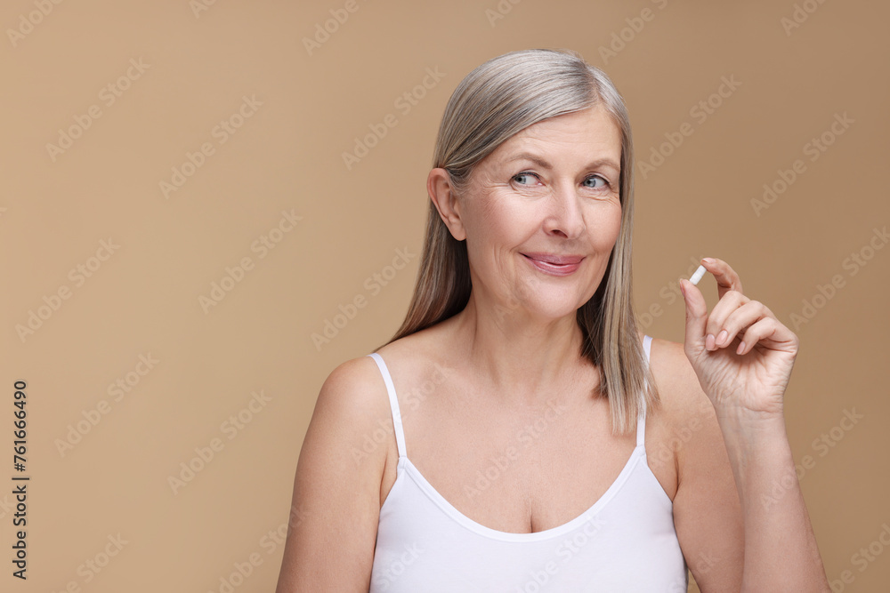 Beautiful woman with vitamin capsule on beige background, space for text Beautiful woman with vitamin capsule on beige background, space for text