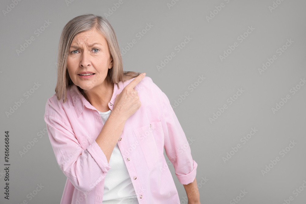 Surprised senior woman pointing at something on grey background, space for text Surprised senior woman pointing at something on grey background, space for text