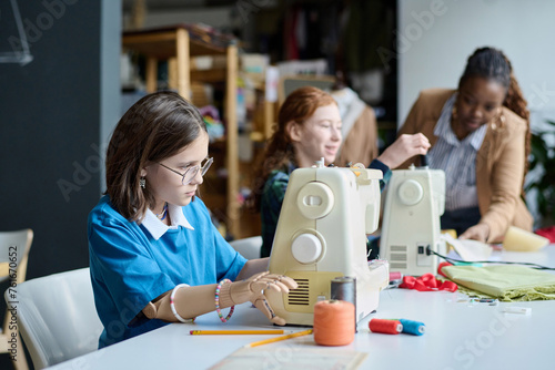 Side view portrait of girl with prosthetic hand using sewing machine in tailoring class photo