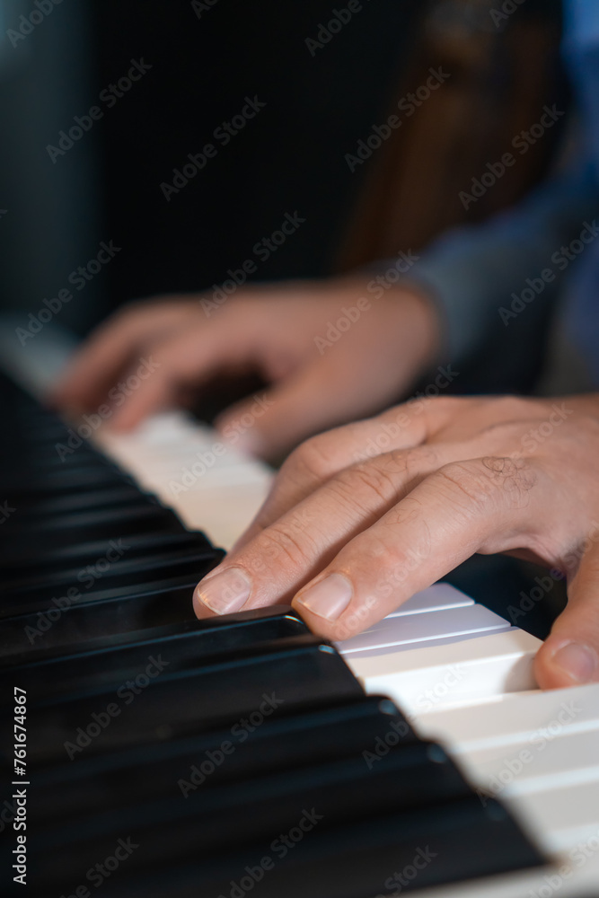 Close-up of male hands playing an electronic piano. Musical education at a music school. Private music lessons with a teacher. Vertical photo