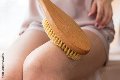 Her delicate hand grips the wooden brush as she gently caresses her leg in a soothing gesture. The soft bristles trace her skin with precision, creating a subtle art on her smooth surface