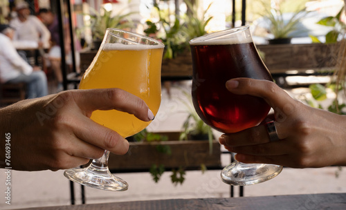 Celebration. Two young women hands toasting with beer cups filled with amber ale and golden honey beer.