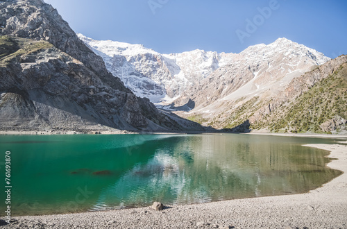 Fototapeta Naklejka Na Ścianę i Meble -  Blue turquoise lake Kulikalon against the backdrop of rocky mountains with glaciers on a warm sunny morning in the Fan Mountains in Tajikistan, landscape in the mountains
