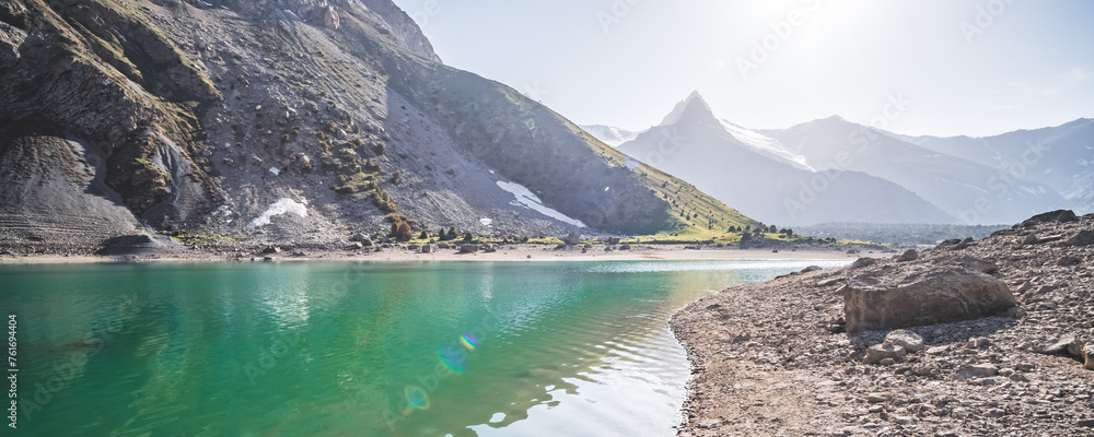 Blue turquoise lake Kulikalon against the backdrop of rocky mountains with glaciers on a warm sunny morning in the Fan Mountains in Tajikistan, landscape in the mountains - obrazy, fototapety, plakaty 