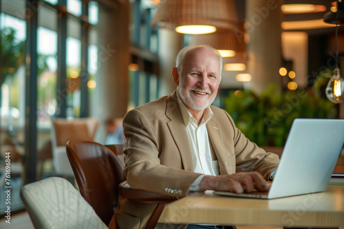 Portrait of a smiling senior businessman using a laptop while sitting at a table in a modern office
