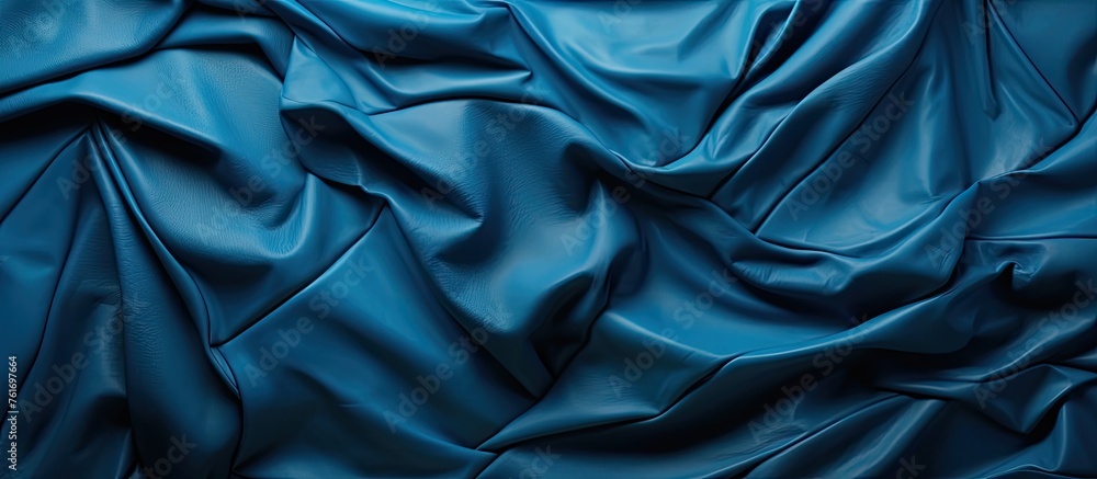 A closeup of electric blue satin fabric with wave patterns resembling the movement of water. The fabric looks luxurious and feels silky smooth to the touch