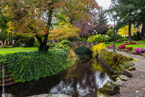 Urban park in autumn season. Decorative stone bridge crossing a water stream